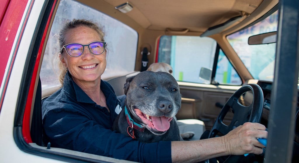 A smiling woman wearing glasses in a vehicle with a dog on her lap